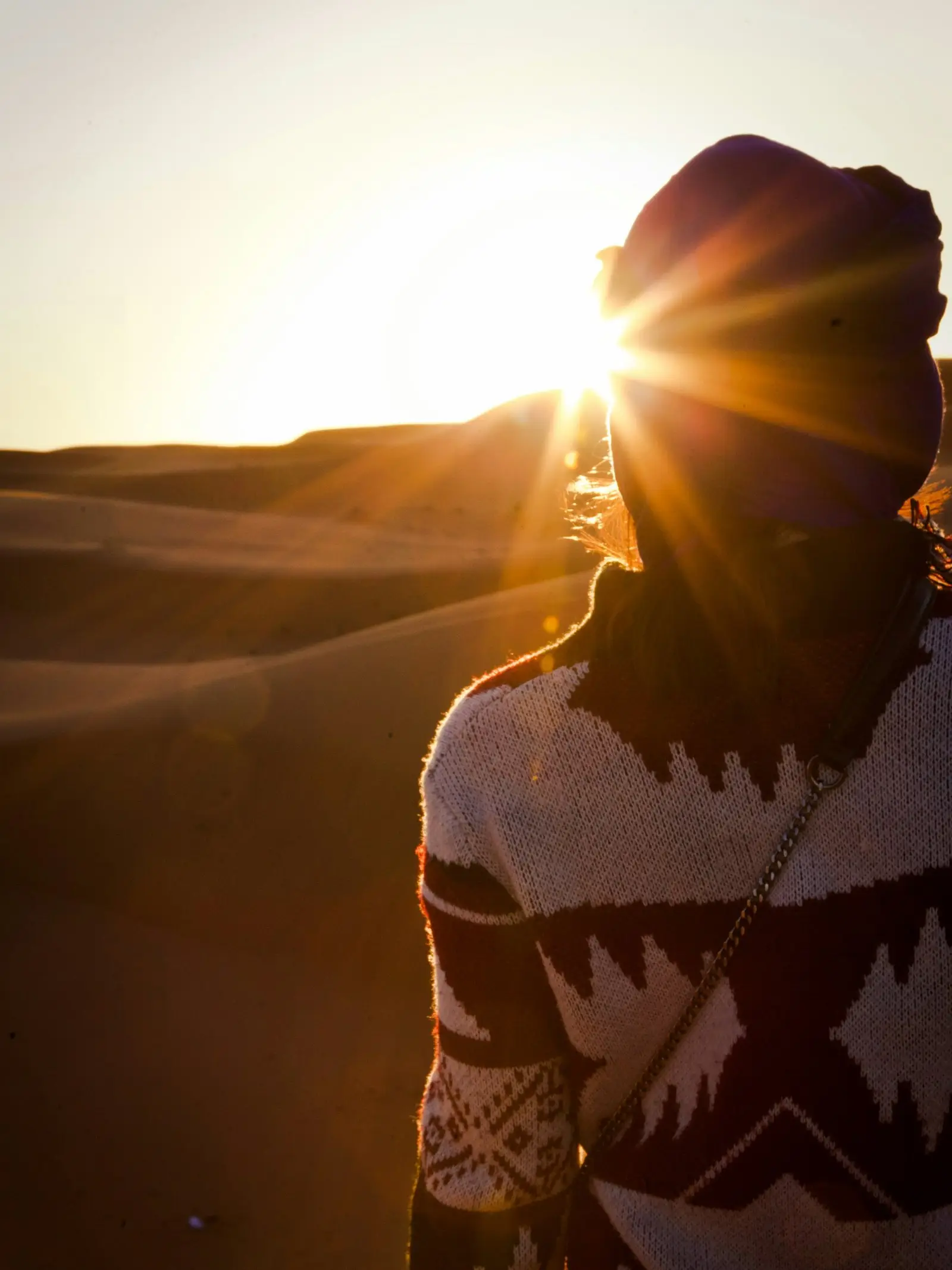 Une femme de dos face au soleil couchant dans les dunes
