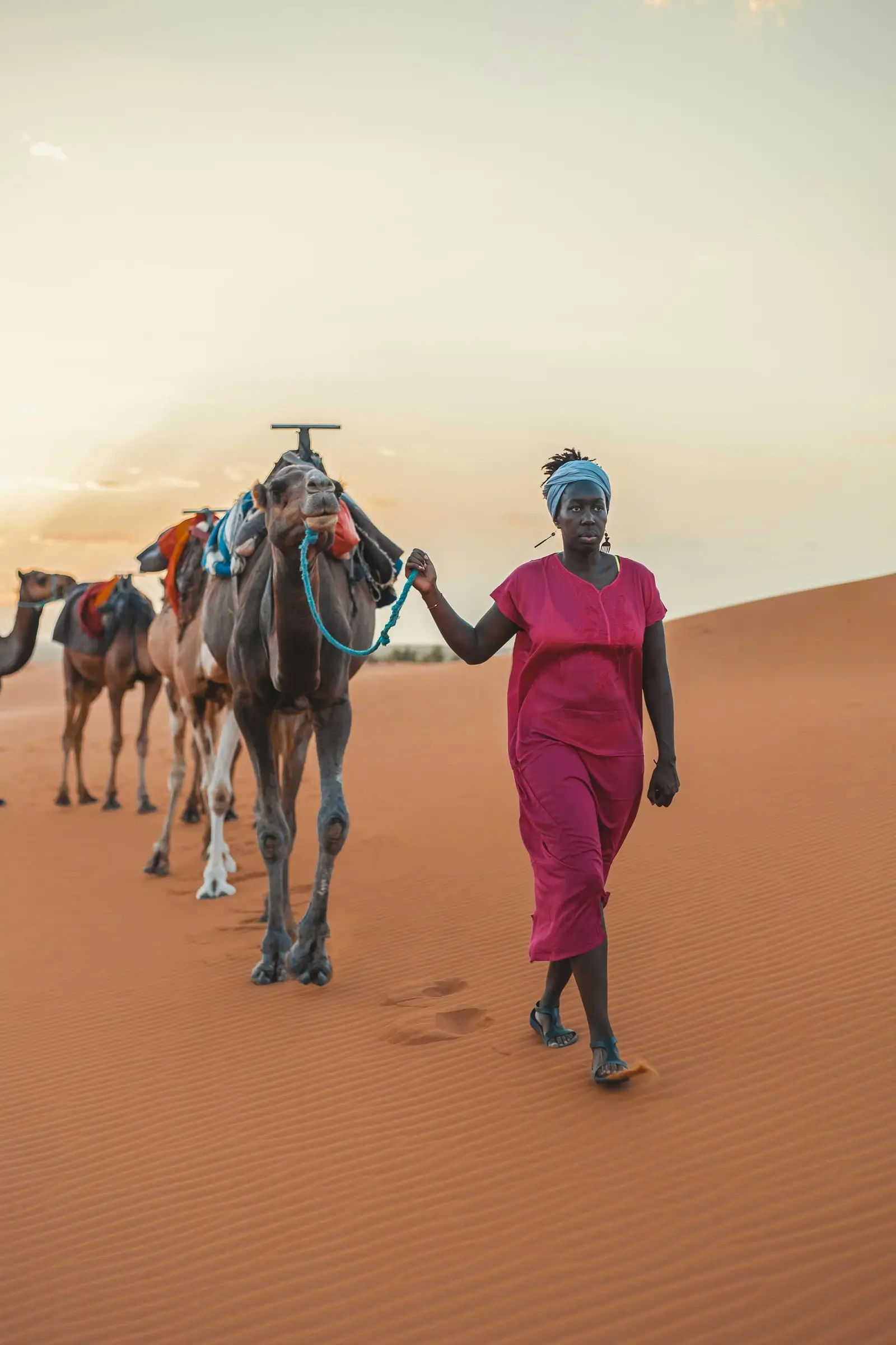 Une femme marche dans les dunes en tenant la corde de dromadaires
